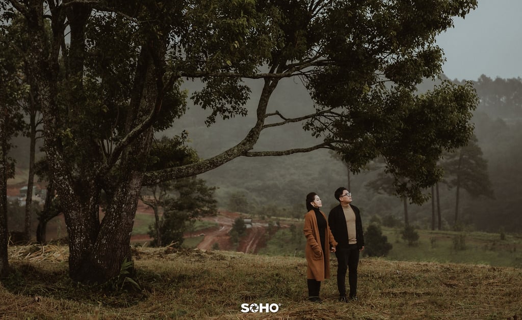 a couple standing in a field with trees in the background