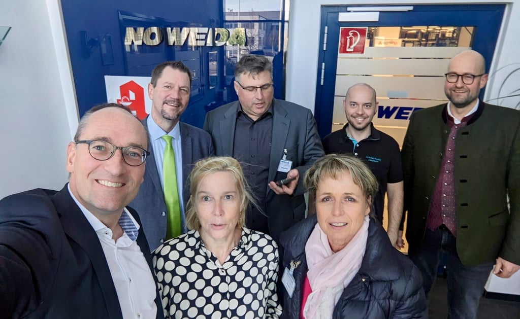Gruppenfoto von sieben Personen in Businesskleidung bei einem Besuch in einem modernen Firmengebäude