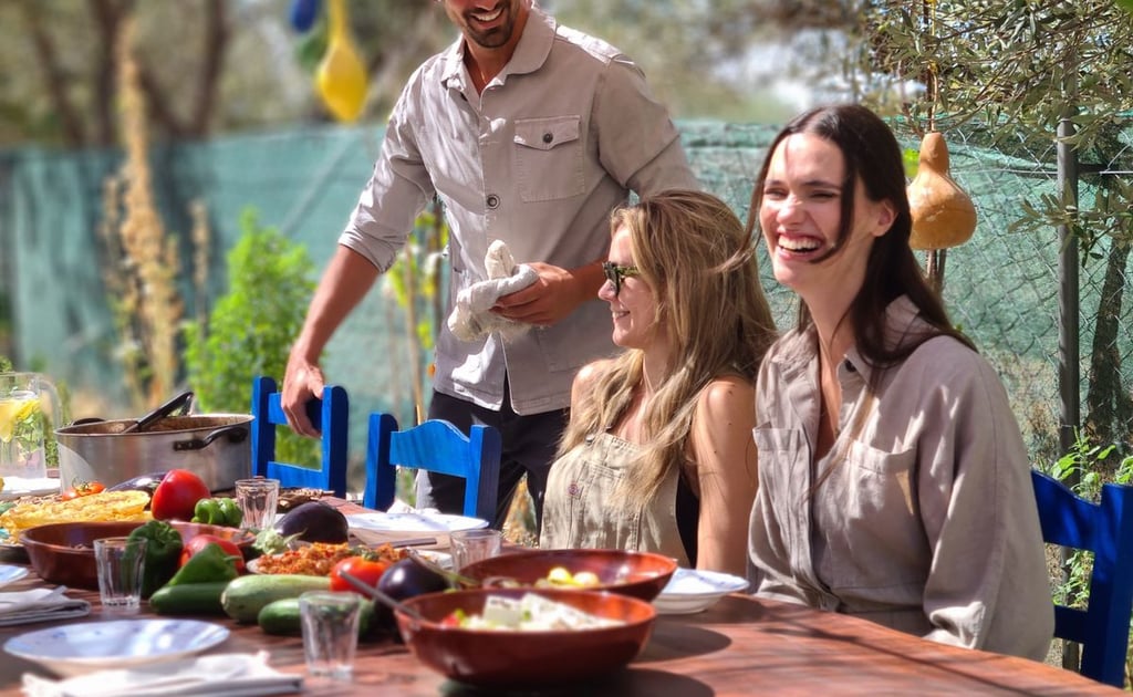 Smiling friends enjoying an outdoor Mediterranean garden lunch with fresh vegetables and rustic decor.