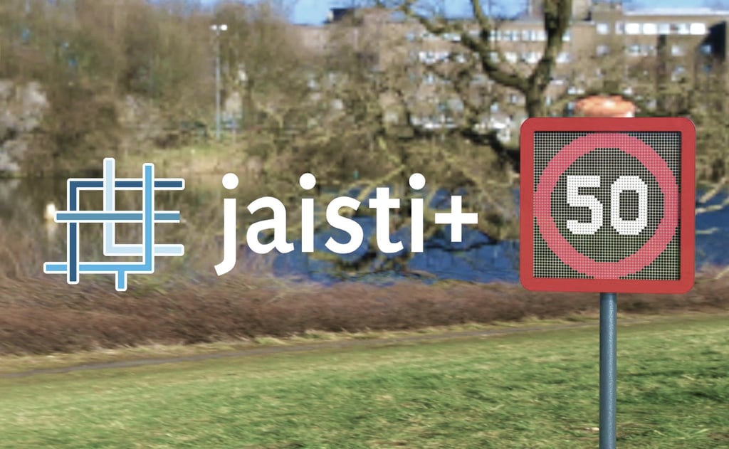 Jaisti+ logo next to a 50 speed limit sign with a blurred park and lake background.