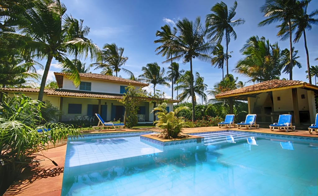 Luxury tropical villa with a private swimming pool, blue lounge chairs, and palm trees.