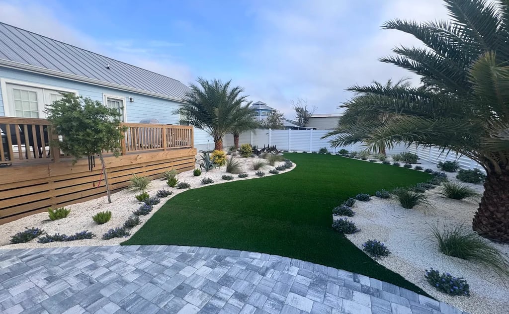 Modern backyard landscaping with artificial turf, palm trees, and a white gravel rock garden.