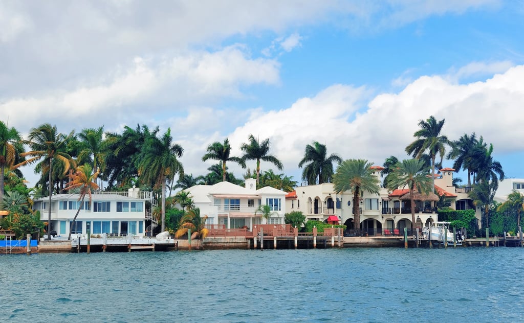Luxury waterfront mansions in Miami Florida with palm trees and boat docks along the blue ocean water.