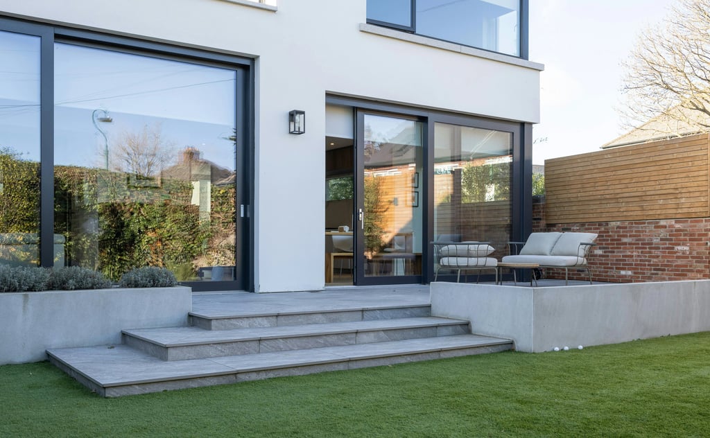 Modern home exterior with black sliding glass doors, stone patio steps, and artificial grass lawn.