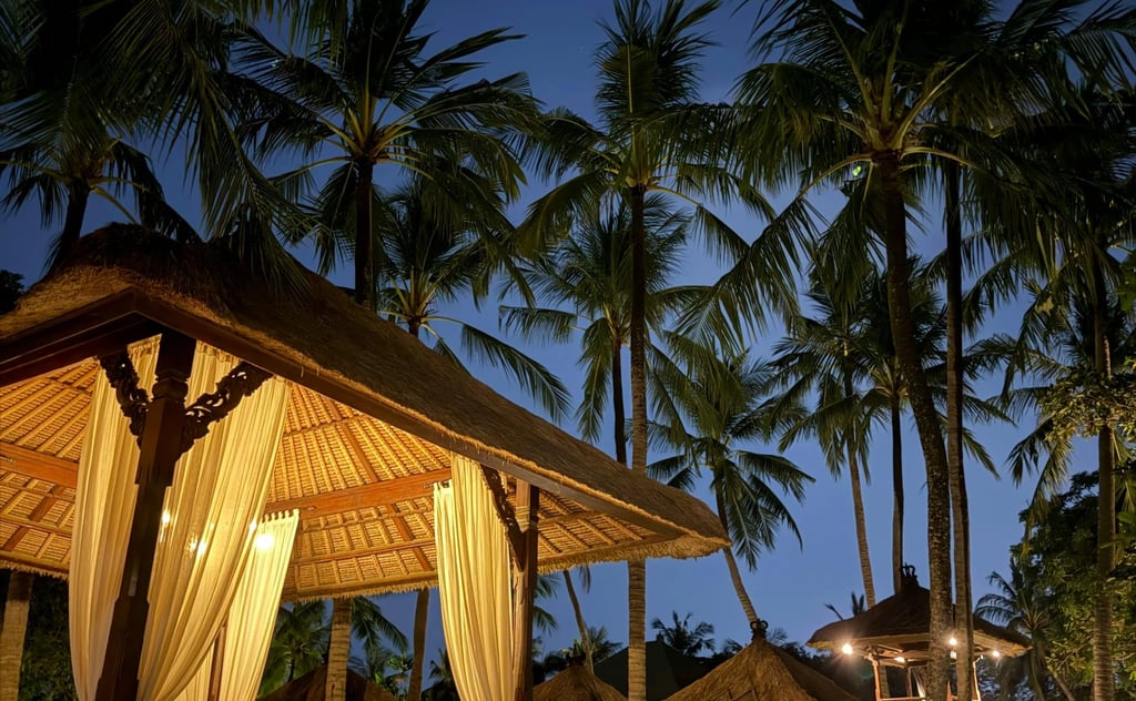 Luxury tropical resort at night featuring illuminated traditional Balinese gazebos and palm trees.