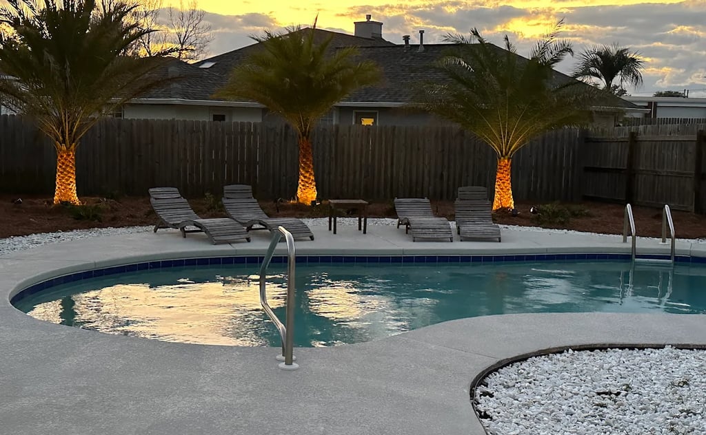 Backyard swimming pool with lounge chairs and lighted palm trees at sunset.