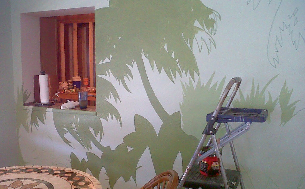 An interior mural underway with a ladder, paint bucket, rags, and tools in the kitchen.