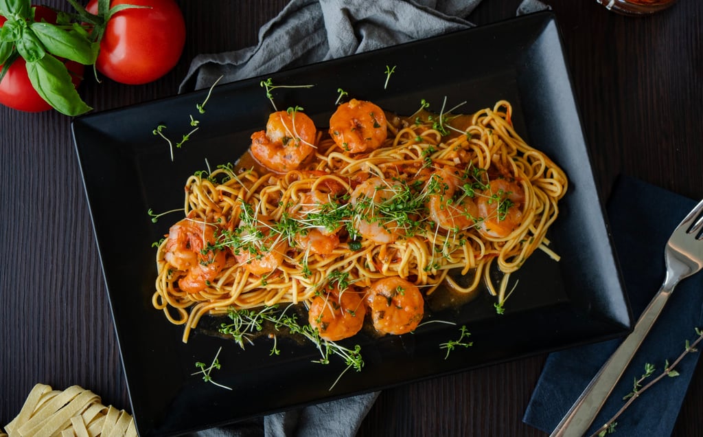 Italienische Pasta mit gebratenen Garnelen, Tomatensauce und frischer Kresse auf schwarzem Teller.
