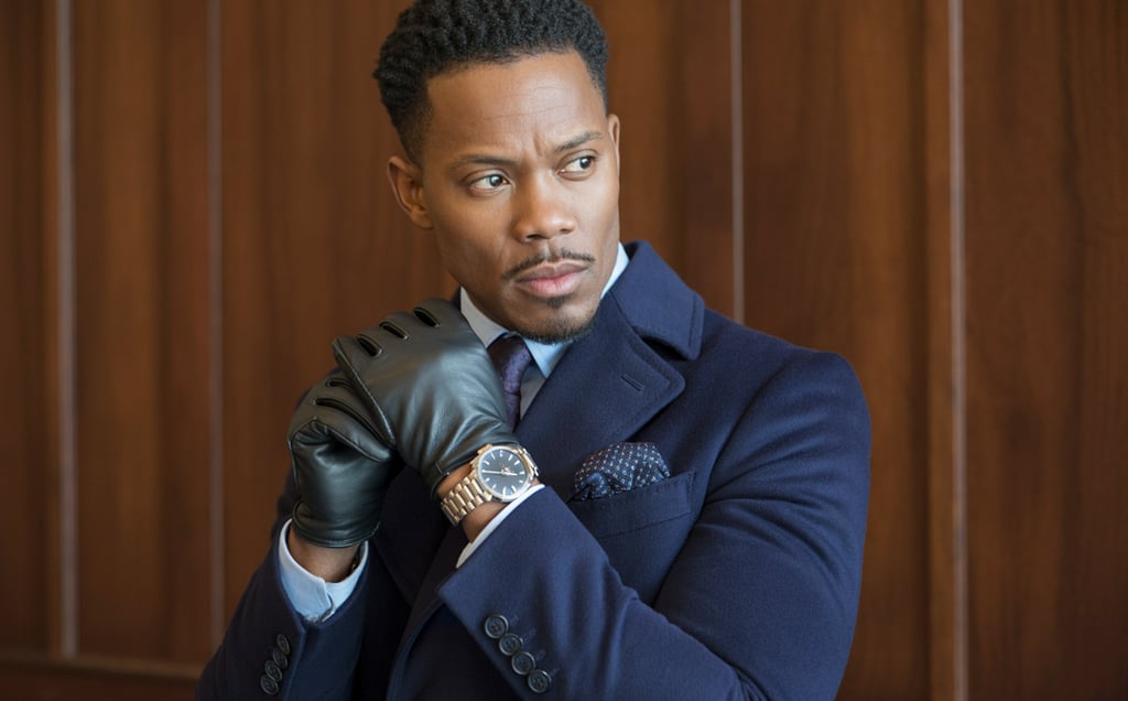 a man in a suit and gloves holding a watch