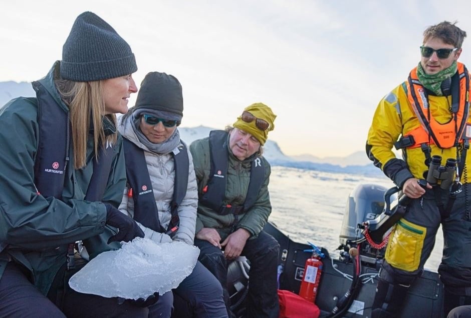 A group of explorers on boat tour, holding a piece of ice, showcasing sustainable polar travel and ecotourism.