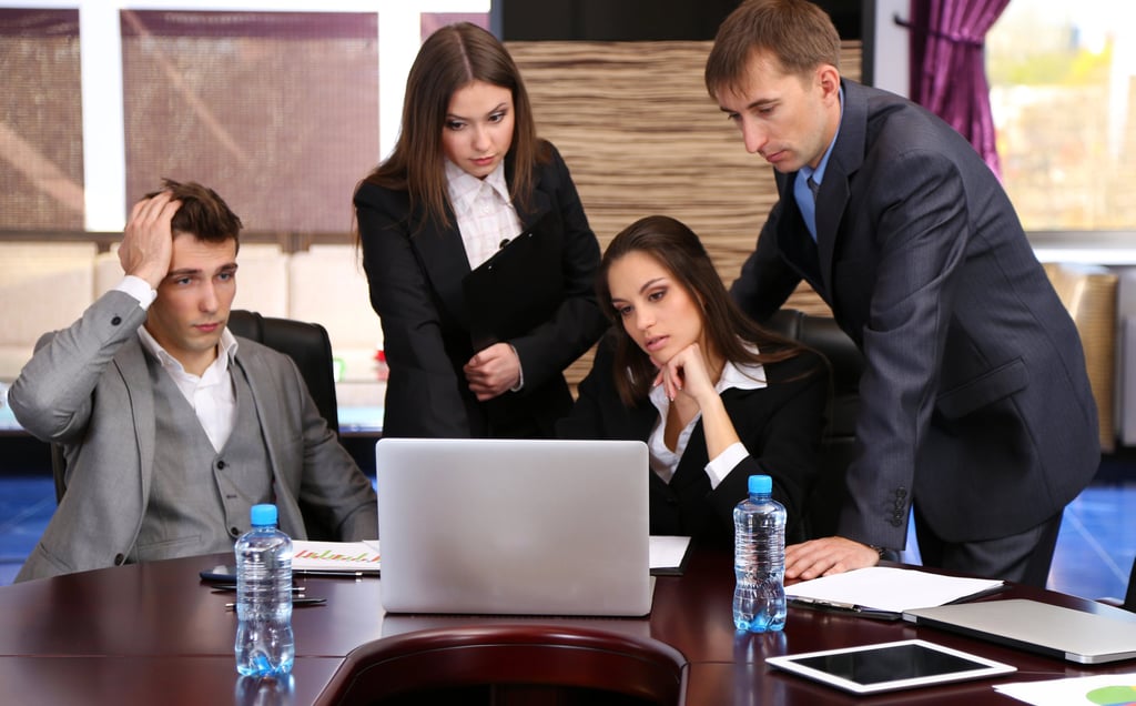 Stressed business team analyzing data on a laptop during a corporate office meeting.