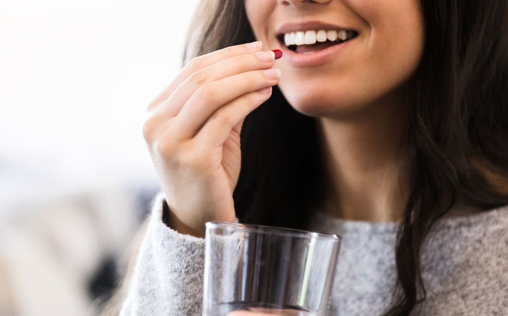 a woman holding a glass of water and taking a vitamin and smiling