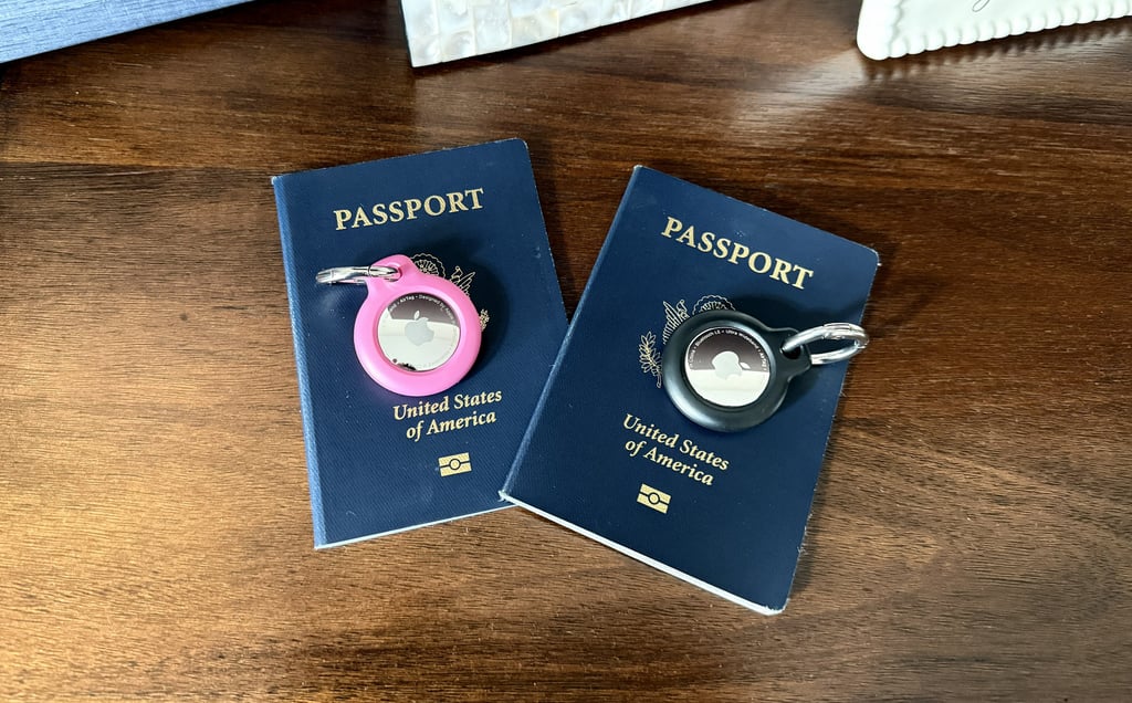 Two AirTags in pink and black placed on our passports for luggage tracking and travel peace of mind