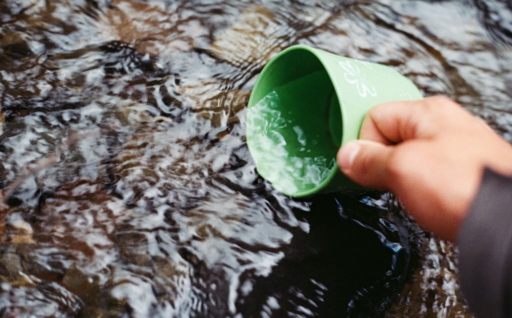 Metal cup collecting river water, representing hydration and water purification outdoors