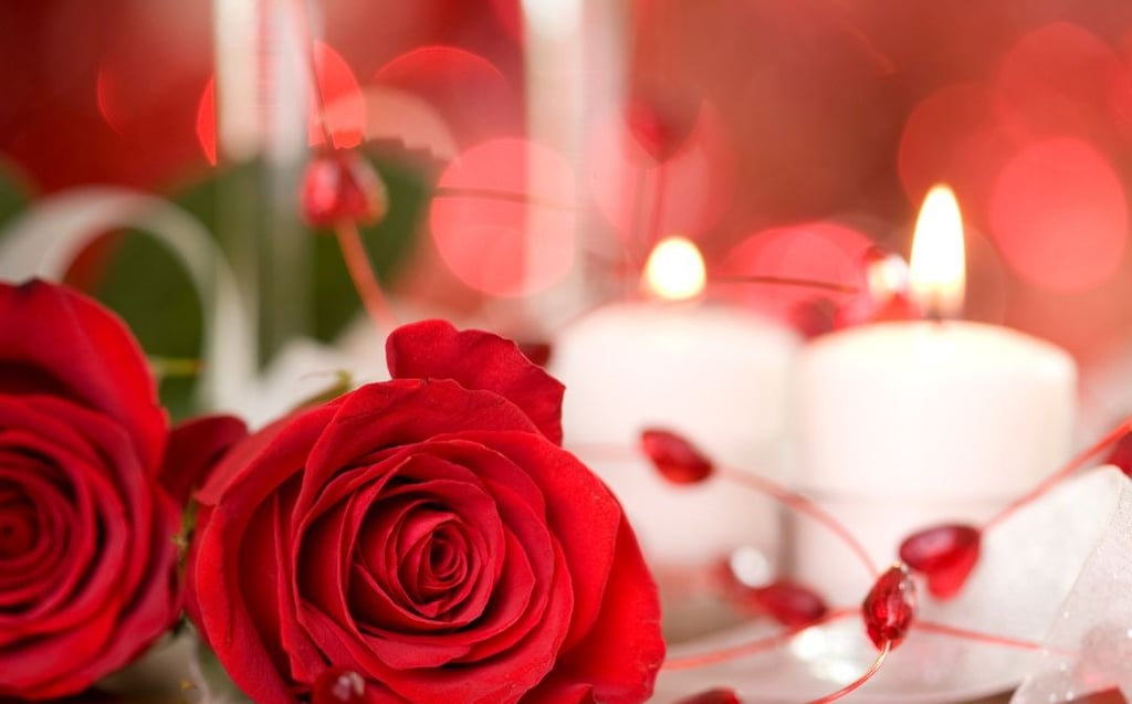 Romantic red roses and lit candles on a table with a red bokeh background for Valentine's Day.