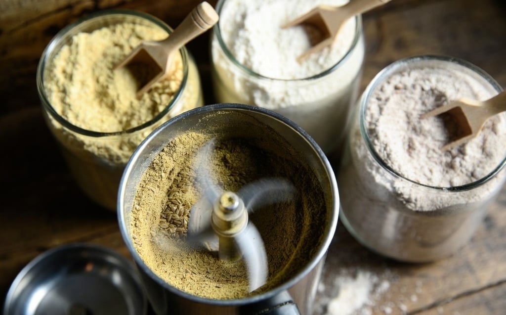 Primer plano de un molinillo de café eléctrico pulverizando semillas de lino dorado hasta convertirlas en polvo