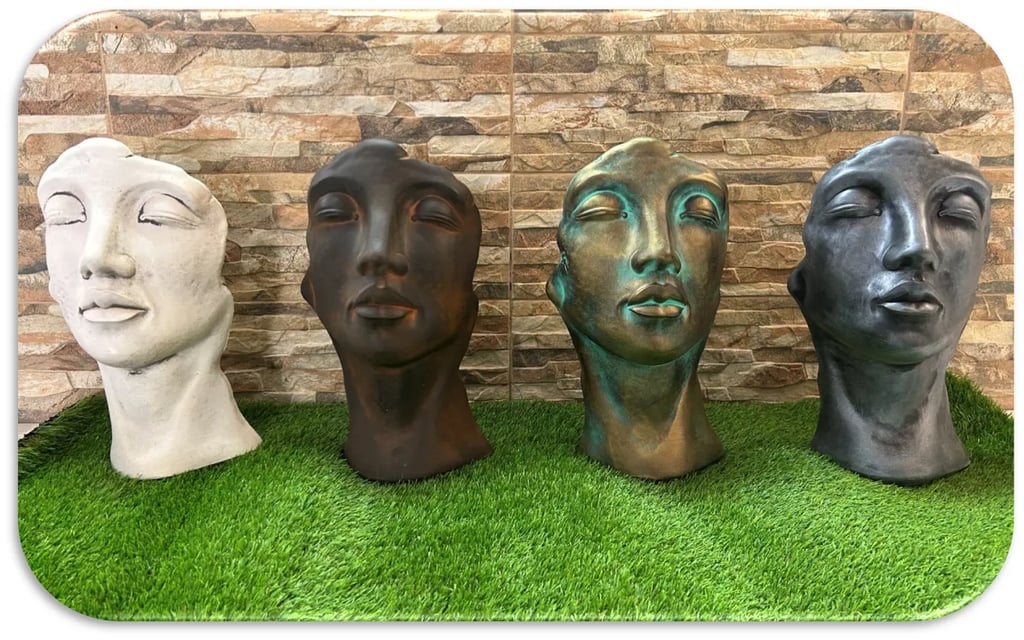 Four face-shaped garden planter pots in different finishes displayed on artificial grass.