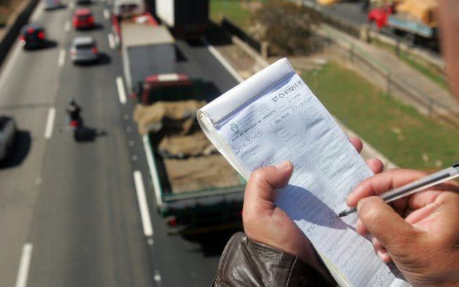 Traffic officer writing a speeding ticket above a busy highway with trucks and cars.