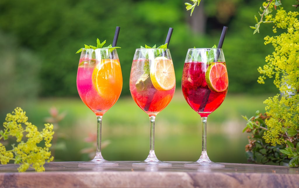 Drei bunte Aperitifs im Freien, Orange, Gelb, Rot. Frische Minze, Limetten & Strohhalme. metta-macro