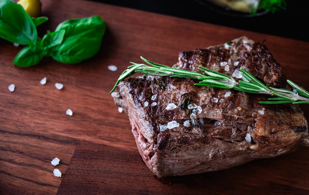 Saftiges gegrilltes Rindersteak mit frischem Rosmarin und grobem Meersalz auf einem Holzbrett