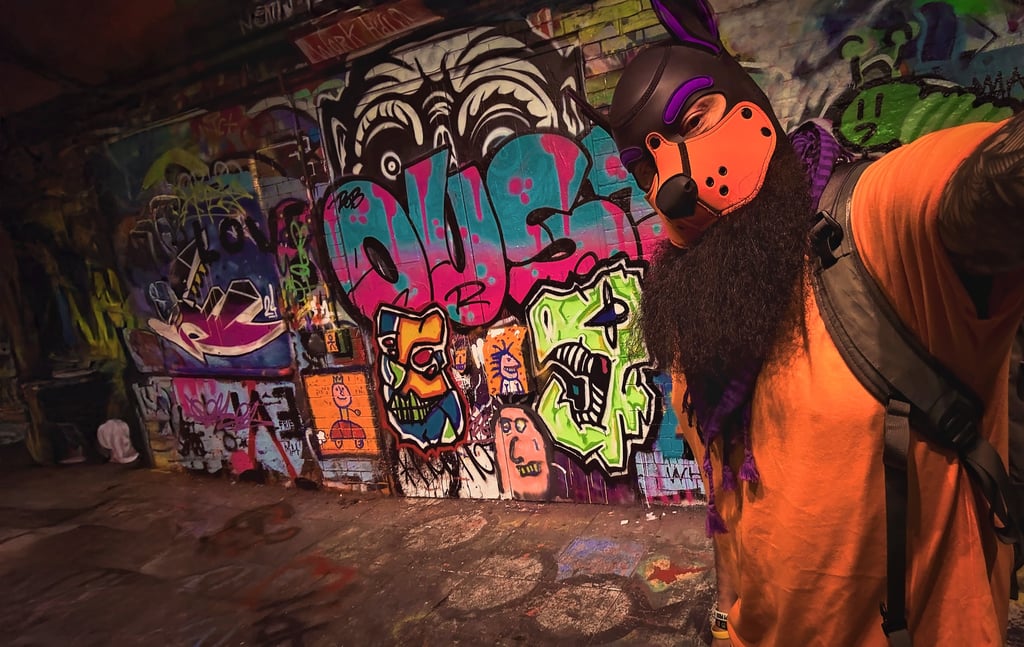 Man in a pup mask posing in front of a graffiti wall.
