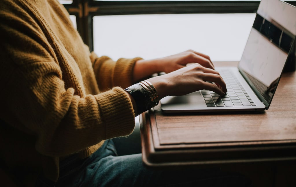 Photograph of a person sat at a desk with their hands on the keyboard of a laptop