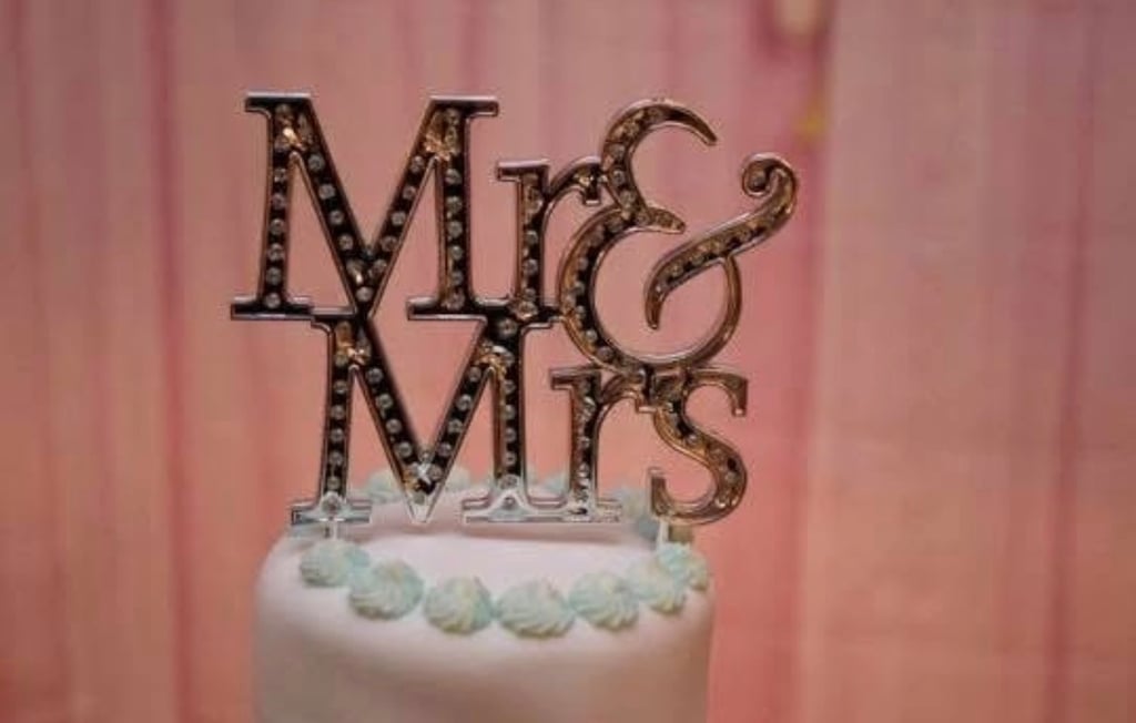 Elegant silver Mr & Mrs wedding cake topper with sparkling crystals on a white tiered cake.
