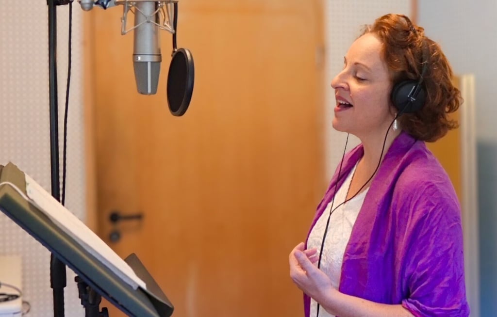 eine Frau mit violettem Schal singt im Tonstudio in ein Mikrofon