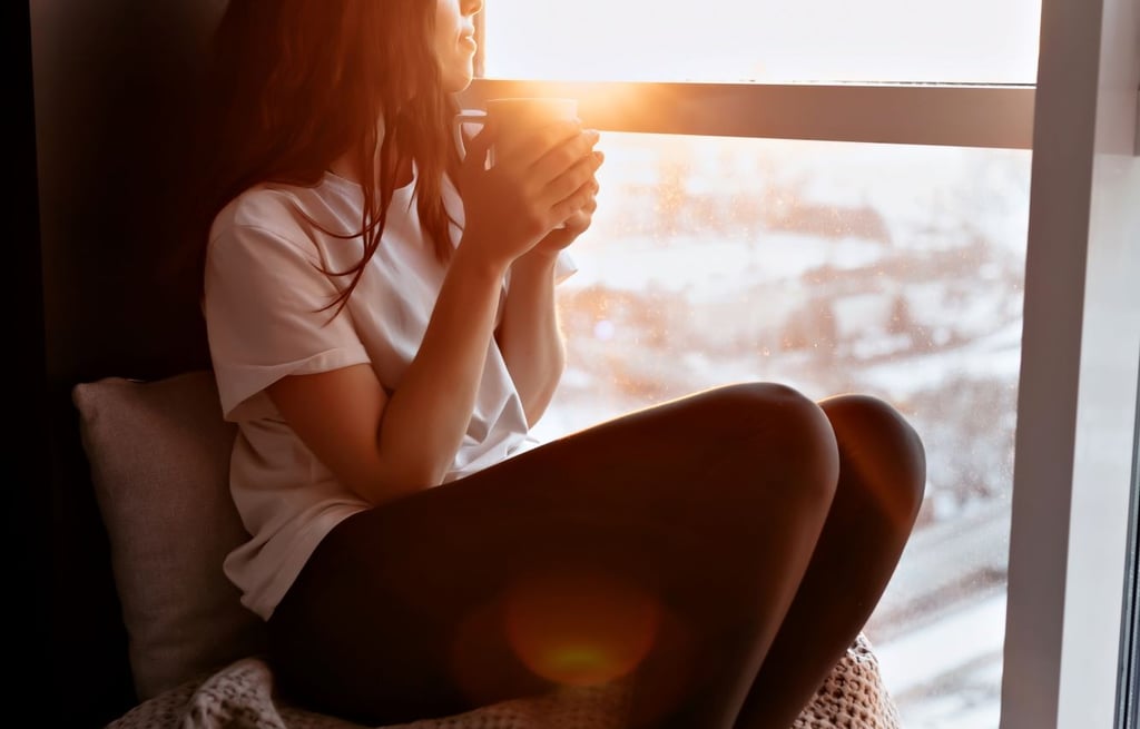 a woman admiring sunrise from room with coffee