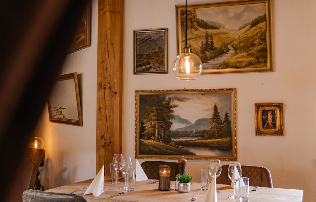 Rustikaler Fine-Dining-Tisch mit Landschaftsgemälden und warmer Kugel-Pendelleuchte.
