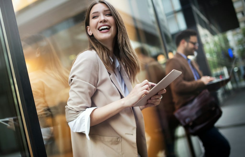 woman in a blazer and white shirt with rolled up sleeves. standing outside, holding a digital tablet