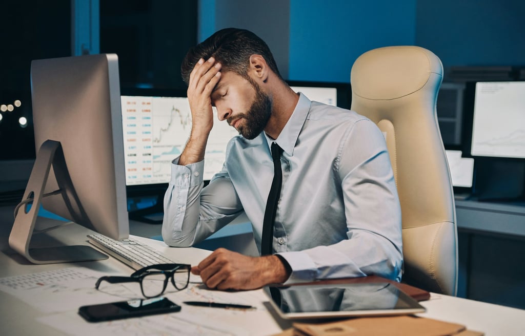 Stressed businessman sitting at his desk, holding his head in one hand