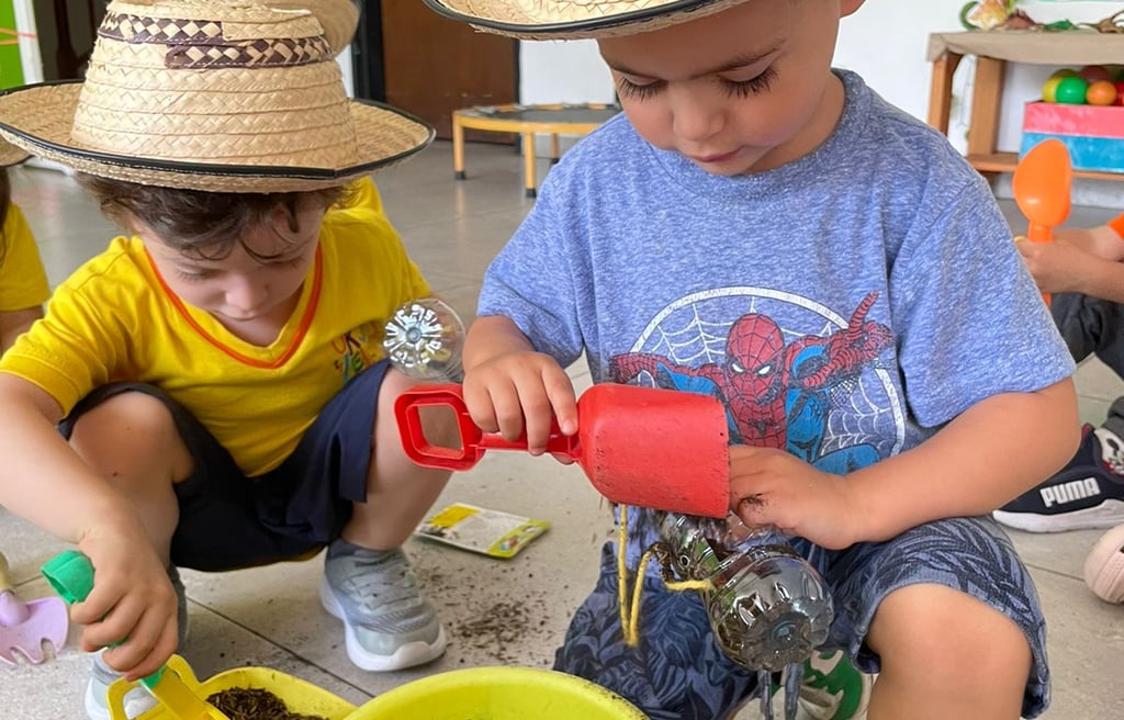 Niños jugando a la jardinería con tierra en baldes amarillos y sombreros campesinos en Jardín infantil Ukelele