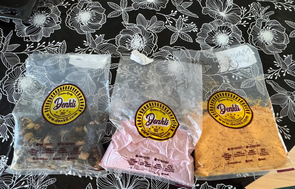 Three bags of Denkli brand organic spice powders and dried goods on a floral tablecloth.