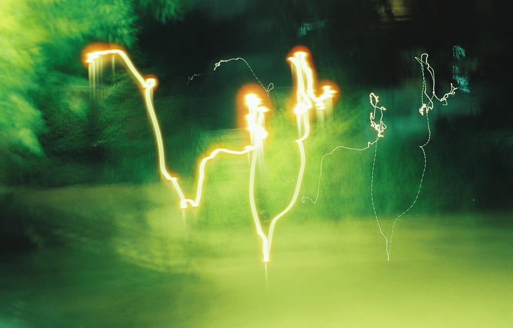 Abstract long exposure photography featuring golden light trails against a blurry green nature background.