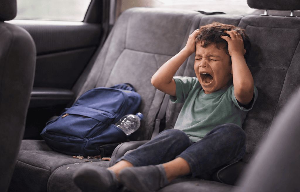 a distressed child in the  back seat with his back pack next to him