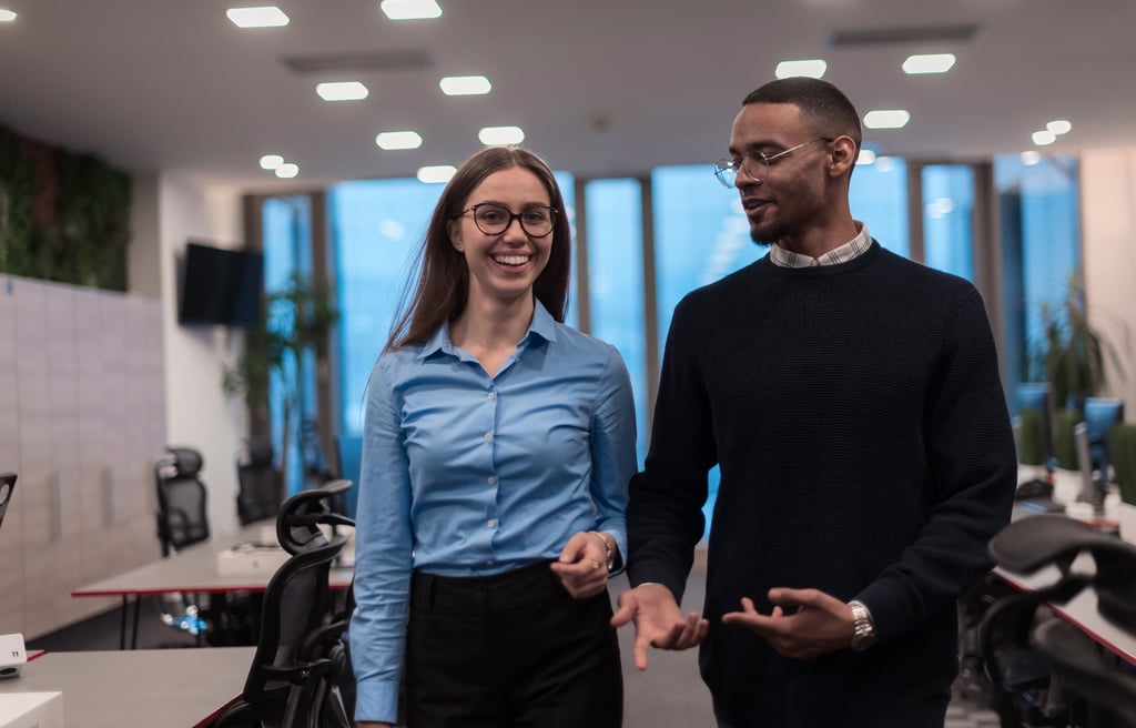 Two diverse young professionals walking and talking in a modern, open-plan office setting.