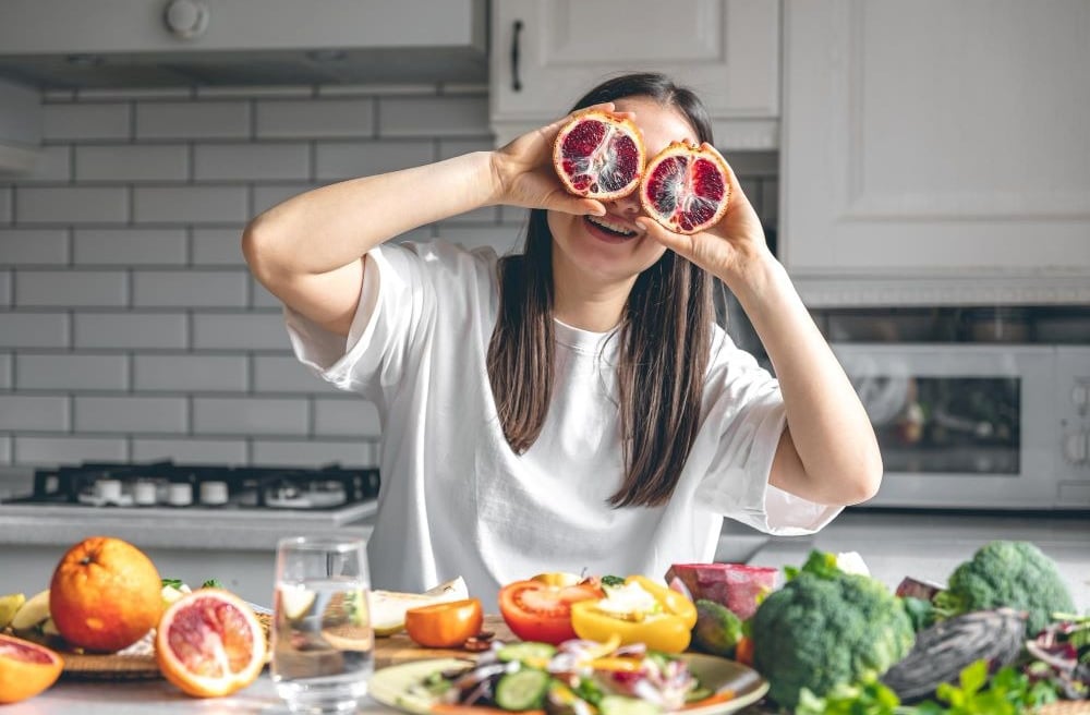 Happy young woman with orange halves in the kitchen