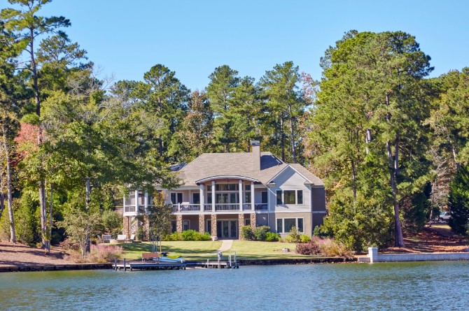 Luxury lakefront home with a private boat dock and manicured lawn surrounded by tall pine trees.