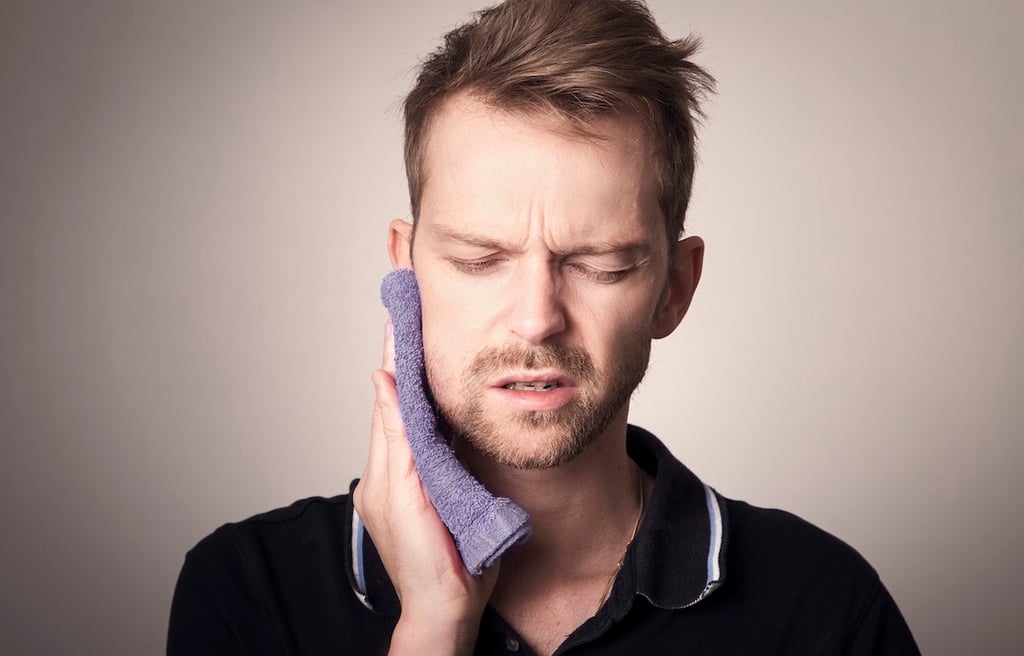 Young man with temporomandibular pain holding his jaw with a towel.