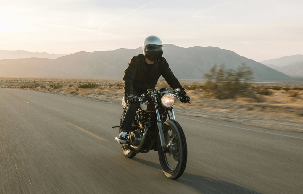 a man riding his cafe racer motorcycle on the road