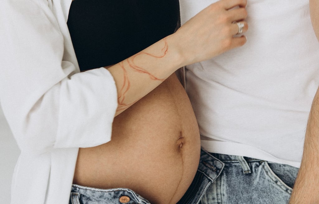 Close-up of a pregnant woman's belly with partner in a maternity photo shoot wearing denim jeans.