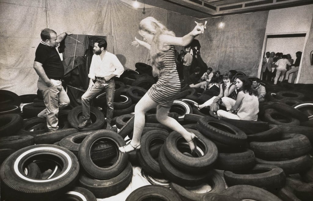 Participantes explorando pilhas de pneus pretos na instalação ‘Yard’ de Allan Kaprow, reconfigurando