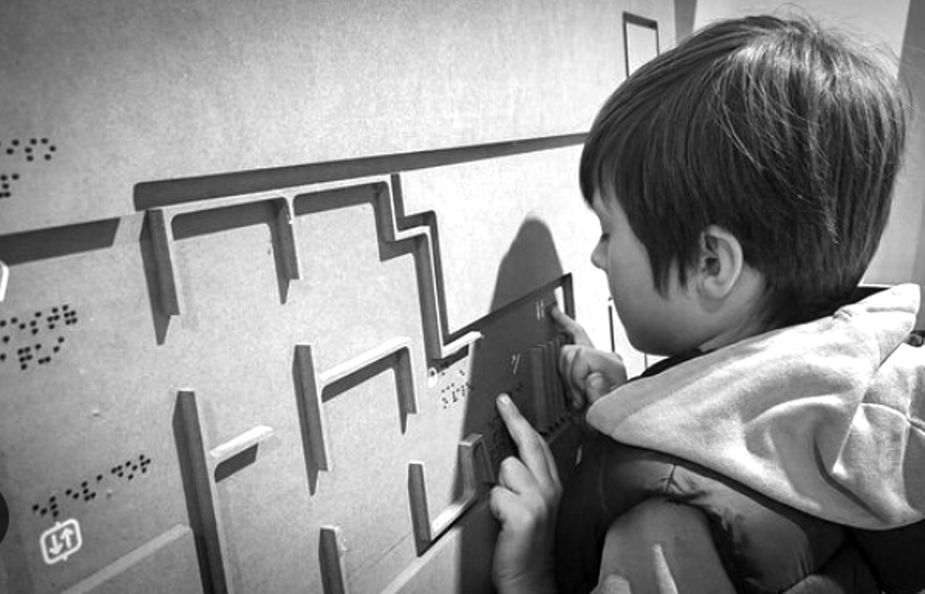 Niewidomy chłopiec odczytuje makietę, na której umieszczono napisy w brajlu