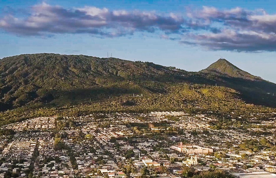 Aerial view of Santa Tec;a nestled at the base of lush green volcanic mountains under a blue sky.