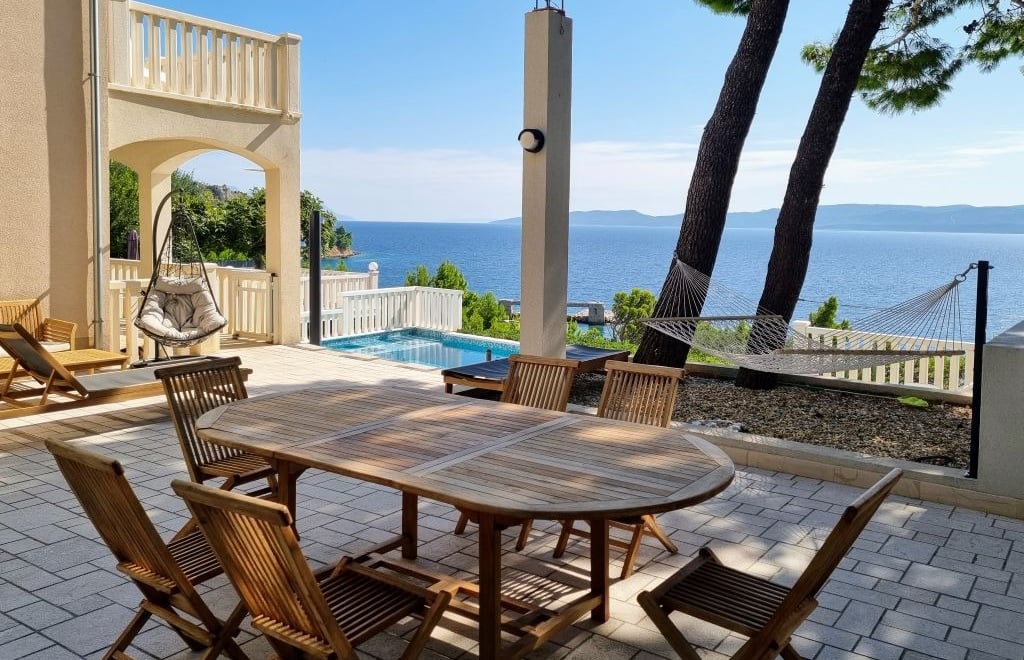 The photo shows a dining table, deck chairs and swings in the central courtyard overlooking the pool and the open sea.