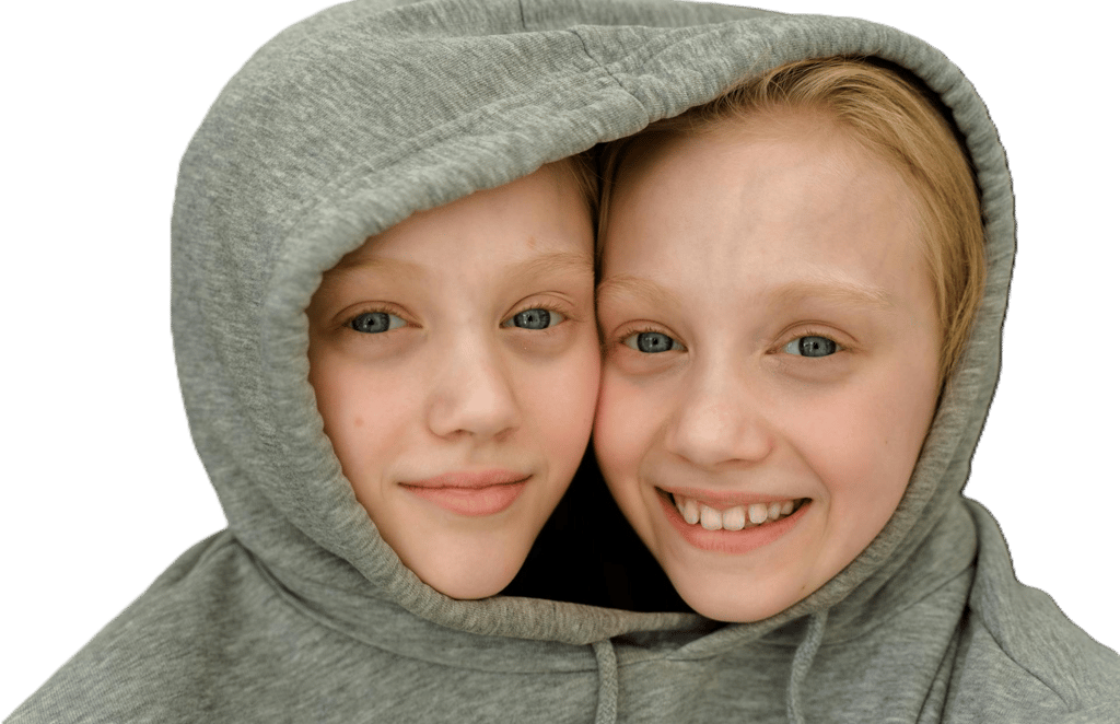 Two smiling girls with blue eyes sharing a single grey hoodie