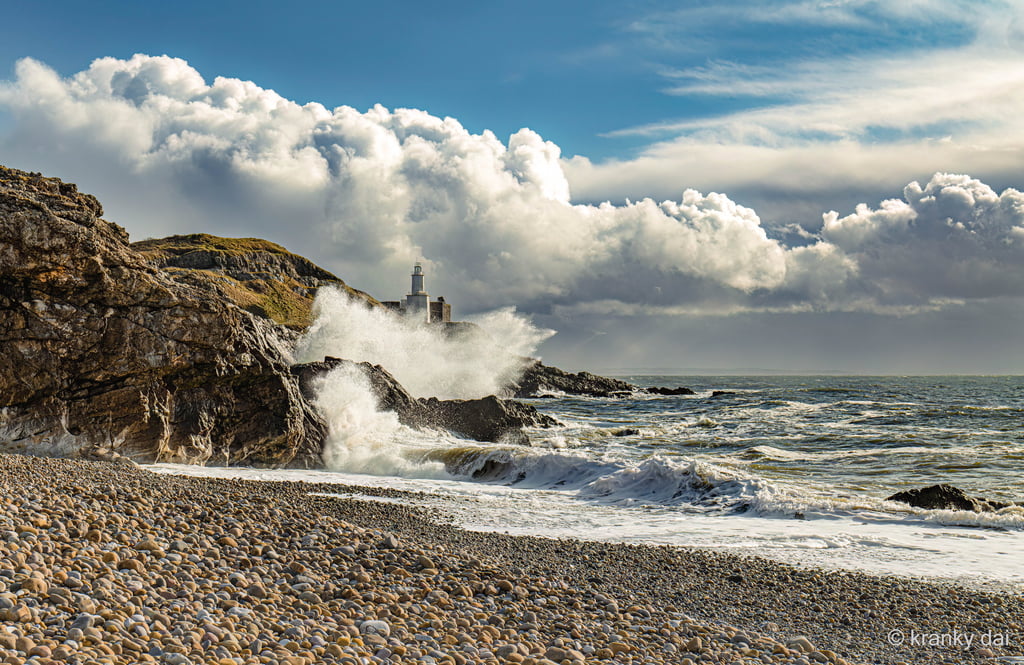 a lighthouse on a rocky beach with waves crashing over the rocks