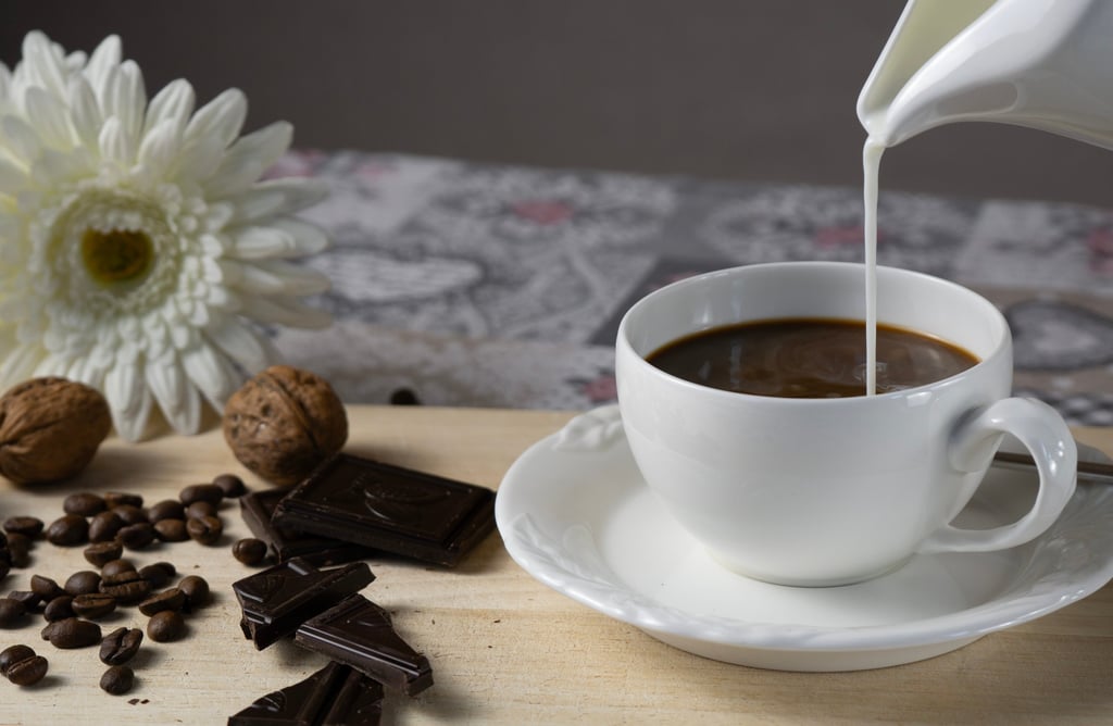 Milch wird eingegossen, Schokolade & Nüsse bereitgelegt. Detailaufnahme für metta-macro