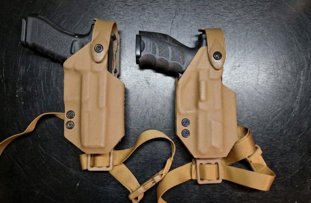 Two black handguns secured in tan kydex tactical holsters with nylon drop leg straps.